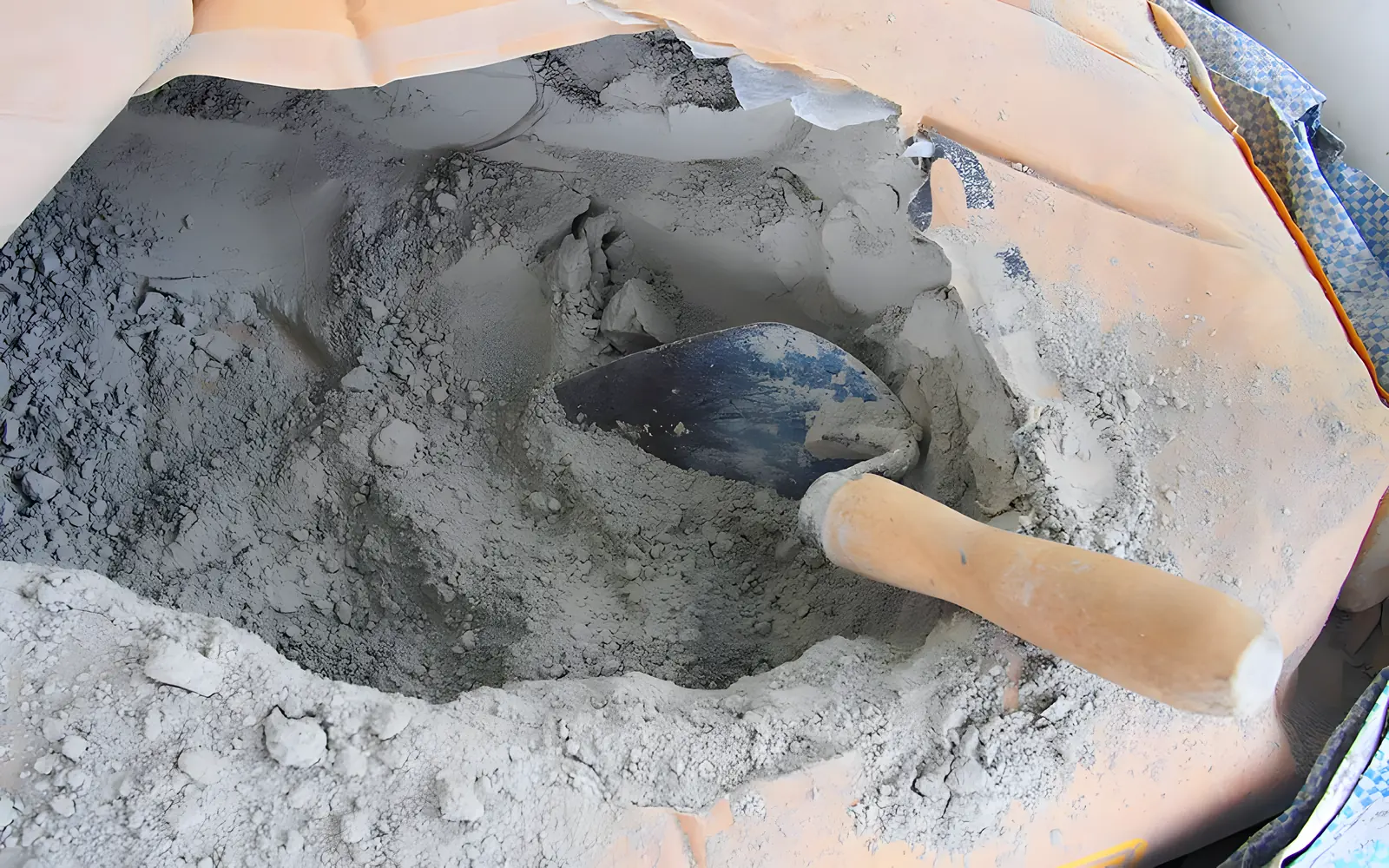 Open bag of grey cement powder with a hand scoop