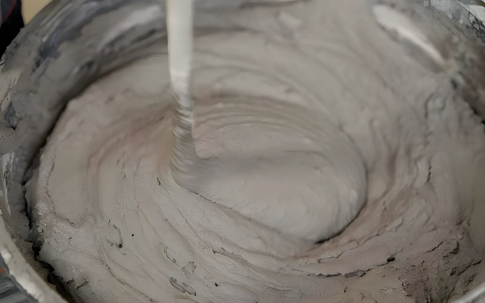 Grey mortar being mixed in a bucket with a paddle mixer